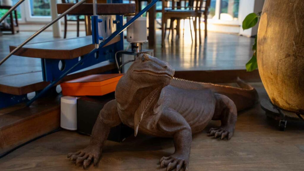 Lebensgroße Echsenfigur unter einer Treppe im Wohnzimmer.