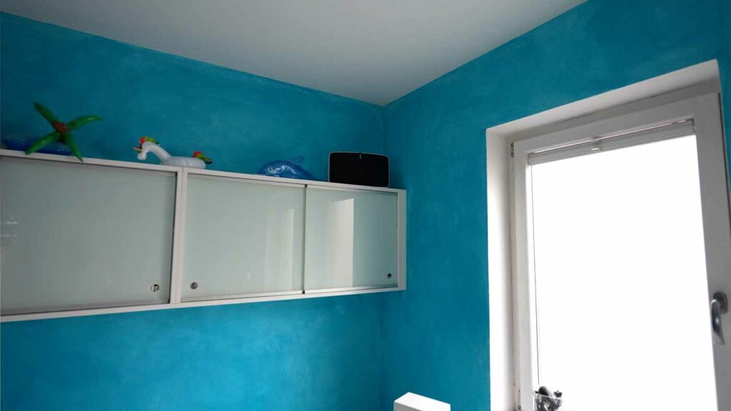 Türkis gestrichene Wand mit weißem Schrank und Fenster.