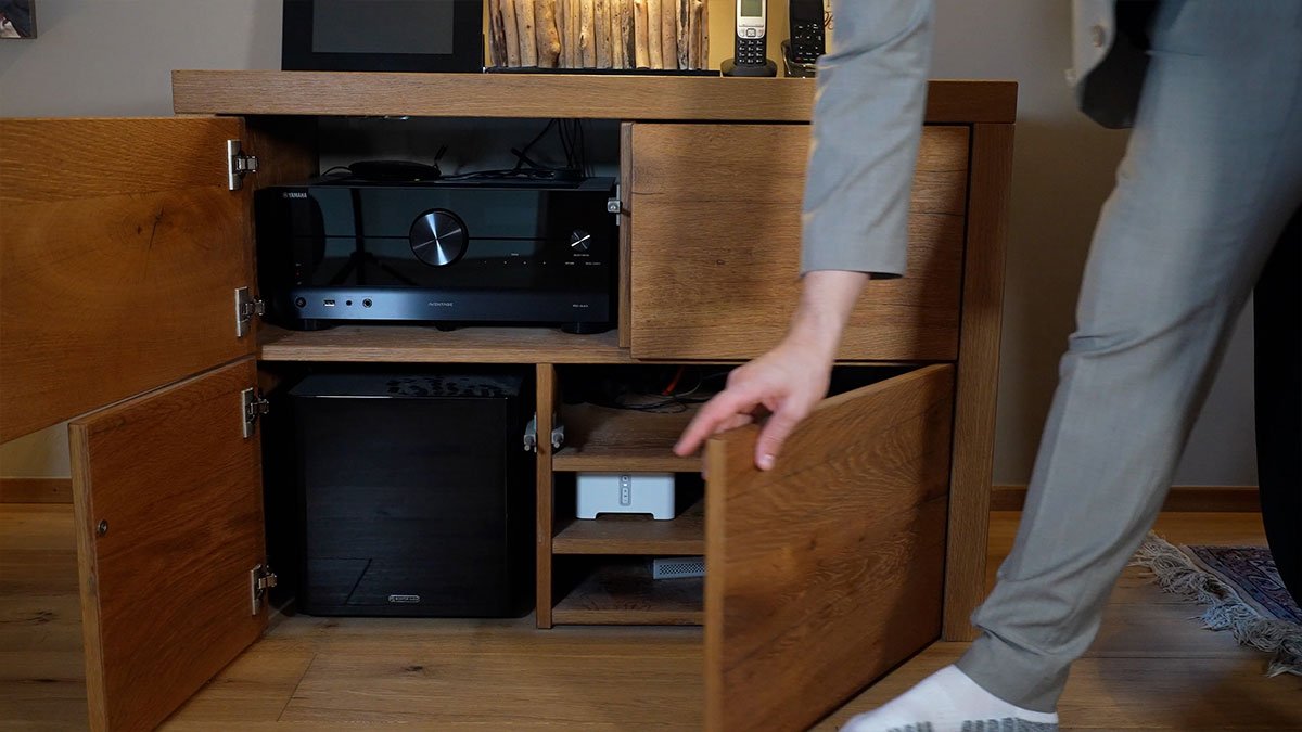 Person öffnet Holzmöbel mit Stereoanlage und Geräten.